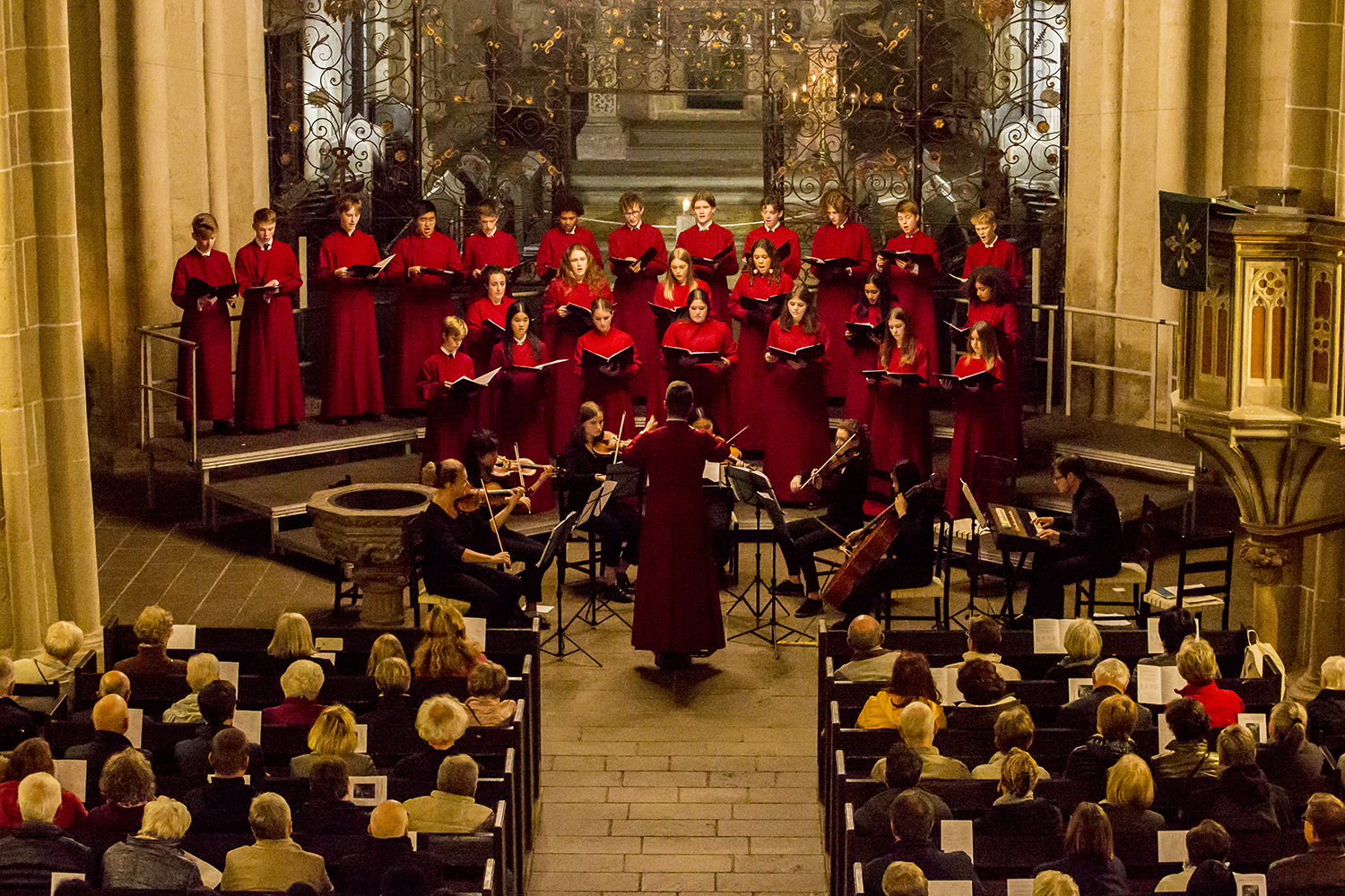 Choir in red cassocks performing with string ensemble to full church