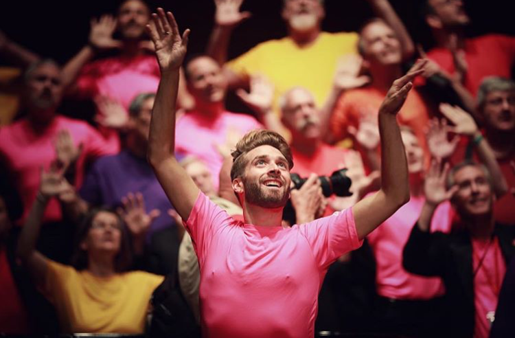 Choir performing with hands raised in colourful t-shirts